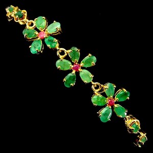 May include: A gold bracelet featuring three flower-shaped links, each composed of five oval-cut green emerald petals surrounding a central round-cut red ruby. The floral links are connected by small gold rings and additional emerald accents.