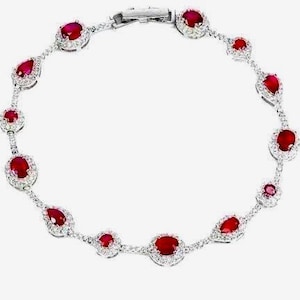 Op de afbeelding: Een zilverkleurige armband met een reeks afwisselend ovale en peervormige dieprode robijnen. Elke robijn is omringd door een halo van kleine, heldere, fonkelende steentjes in een fijne metalen ketting met een veilige sluiting.