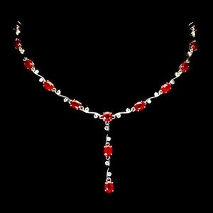 Puede incluir: Un collar de tono plateado que presenta una serie de piedras preciosas rojas de forma ovalada y pequeñas piedras transparentes. El diseño incluye un elemento central colgante con dos piedras rojas adicionales, unidas por una cadena metálica ondulada.