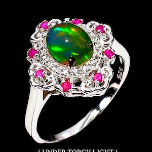 Peut inclure: Bague en argent ornée d'un opale ovale irisée, aux reflets verts et bleus. Elle est entourée de petites pierres roses et de pierres claires. L'ensemble est mis en valeur sur un fond noir. Bijou élégant et raffiné.