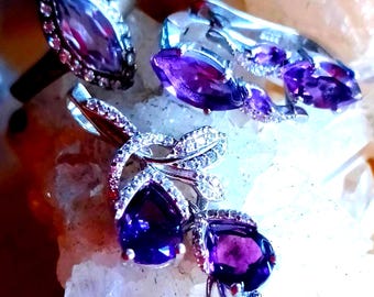 May include: A jewelry set consisting of a ring, a pair of earrings, and a pendant, all crafted from silver-toned metal. Each piece features deep purple marquise and pear-cut stones surrounded by small, clear, sparkling accent stones.