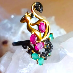 May include: A gold ring with a squirrel design, featuring red and green gemstones. The squirrel's tail is curled up and has black gemstones.