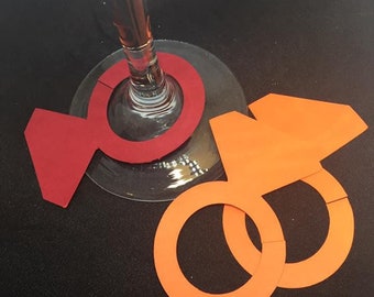 May include: Two wine glass charms, one red and one orange. The red charm is shaped like a candy, and the orange charm is shaped like a ring.