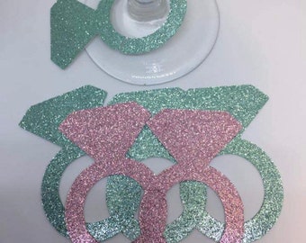 May include: Set of six glitter ring shaped wine glass charms in pink and green. The charms are designed to be placed around the stem of a wine glass to help identify drinks.