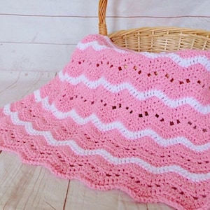 May include: A pink and white crocheted baby blanket with a wavy pattern. The blanket is made with a soft yarn and has a delicate, lacy look.