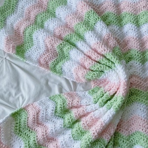 May include: A crocheted baby blanket with a chevron pattern in shades of pink, green, and white.