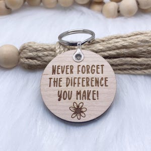 May include: Wooden keyring with a silver ring and the text "Never forget the difference you make!" with a small flower design.