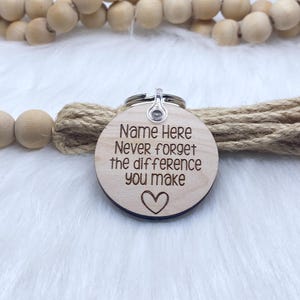 May include: Wooden keychain with a heart and the text "Name Here Never forget the difference you make".