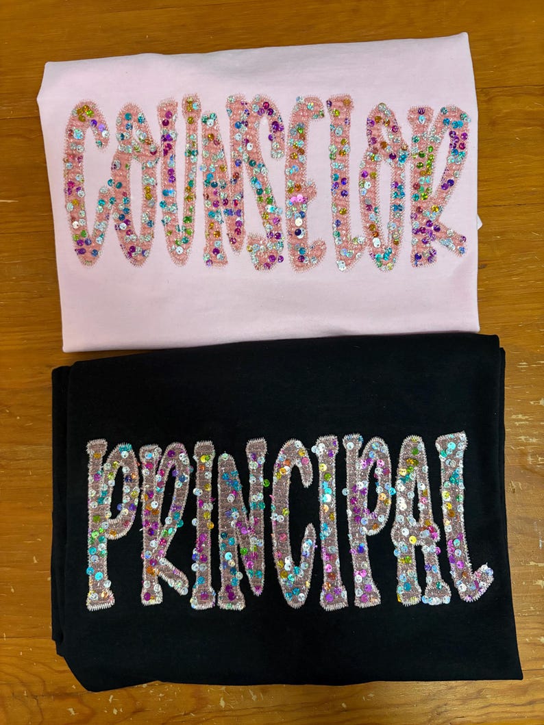 May include: A light pink t-shirt with the word COUNSELOR in multicolored sequin letters and a black t-shirt with the word PRINCIPAL in multicolored sequin letters. Both shirts feature embroidered borders around each individual letter.