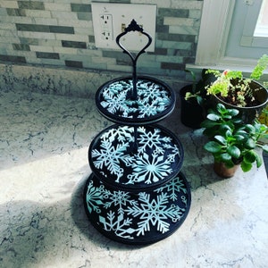 May include: A three-tiered black serving stand with a snowflake design. Each tier is decorated with white snowflakes on a black background.
