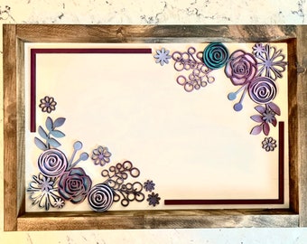 May include: A framed artwork with a white background and a decorative floral design in shades of purple, teal, and gray. The flowers are layered and create a 3D effect.