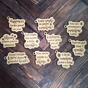 May include: A collection of wooden cutouts with inspirational quotes and phrases. The phrases include "Happiness looks good on you," "Your smile is pure sunshine," and "You are someone's sunshine today." The cutouts are on a dark wood surface.