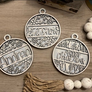 Puede incluir: Tres adornos navideños de madera blanca con un diseño de copo de nieve. Un adorno dice "Let it snow", otro dice "Merry Christmas" y el tercero dice "Andrea".