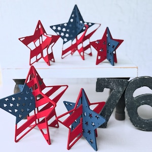 Op de afbeelding: Een verzameling rood, wit en blauw gekleurde sterdecoraties. De sterren zijn gemaakt van metaal en hebben een gestreept en sterrenmotief. Deze patriottische decoraties zijn perfect voor nationale feestdagen.
