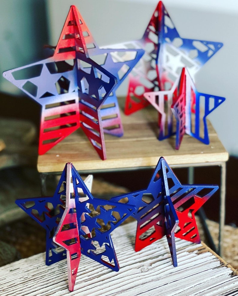 May include: Four wooden stars painted in red, white and blue with a patriotic theme. The stars are layered and have a 3D effect.
