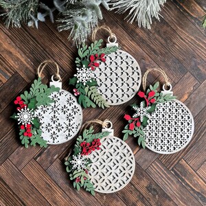May include: Four white wooden Christmas ornaments with a geometric pattern and green and red floral accents.