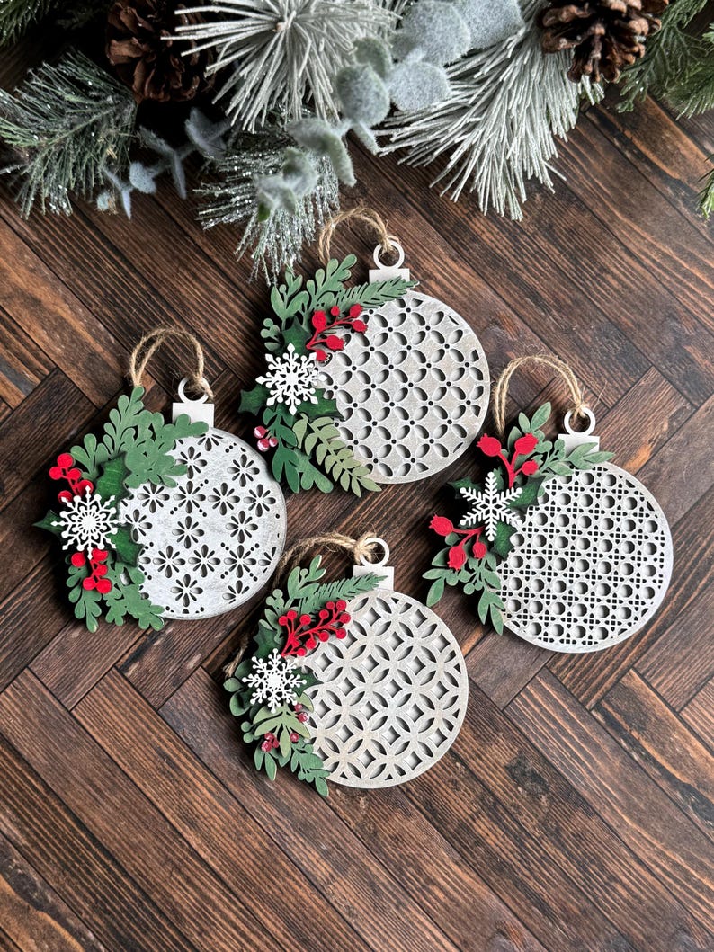 May include: Four white wooden Christmas ornaments with a geometric pattern and green and red floral accents.