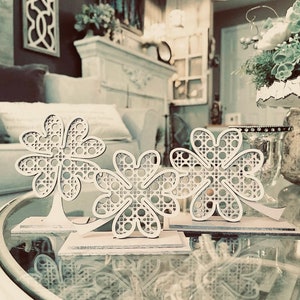 May include: Two white wooden four-leaf clover decorations with a lattice design. The clovers are on a white table with a glass top.