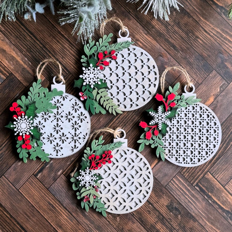May include: Four white wooden Christmas ornaments with a geometric pattern and red and green floral embellishments.