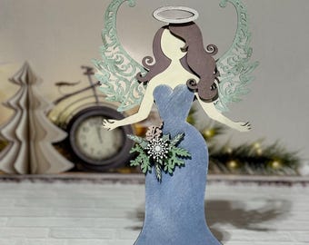 Op de afbeelding: Een houten engelbeeld met blauwe vleugels, een blauwe jurk en een halo. De engel houdt een boeket witte en groene bloemen vast.