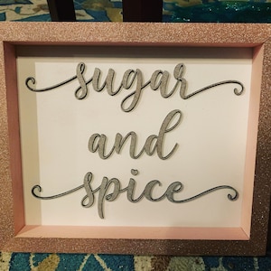 Puede incluir: Un letrero enmarcado con purpurina rosa con las palabras "sugar and spice" escritas en cursiva sobre un fondo blanco.