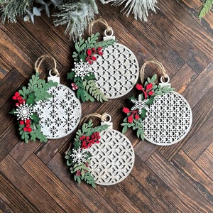 May include: Four white wooden Christmas ornaments with a lacy design and green and red floral accents.