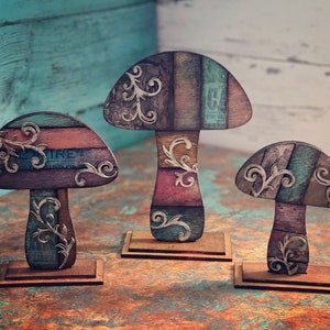 Puede incluir: Tres figuritas decorativas con forma de hongo con un diseño de patchwork colorido y detalles florales. Los hongos están hechos de madera y tienen un aspecto rústico y vintage.