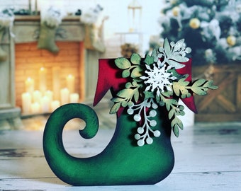 May include: A green elf shoe with a red cuff and a white snowflake and green foliage decoration.