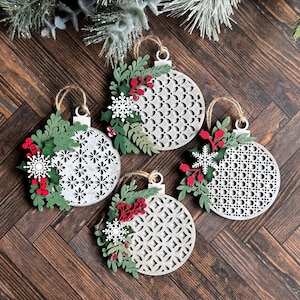 May include: Four white wooden Christmas ornaments with a geometric pattern and green and red paper foliage accents.