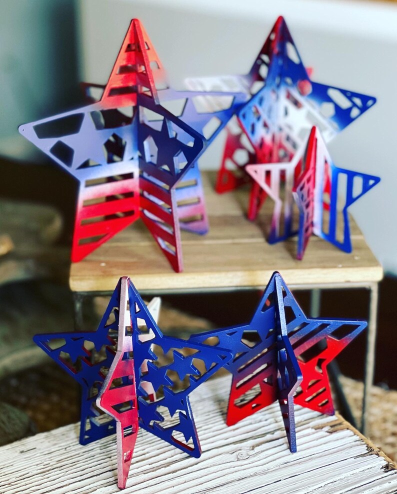 May include: Five red, white and blue wooden stars with a cutout design. The stars are painted with a gradient of red, white and blue.
