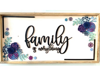 May include: A framed wooden sign with the words "family is everything" in black script. The sign is decorated with purple, blue, and green paper flowers.