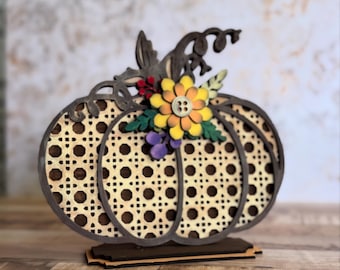 May include: Wooden pumpkin decoration with a woven pattern and dark brown trim. The pumpkin is adorned with a yellow and orange flower, green leaves, and small purple berries. It stands on a wooden base.