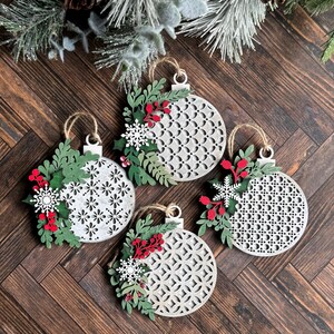 May include: Four white wooden Christmas ornaments with a geometric pattern and red and green floral accents.