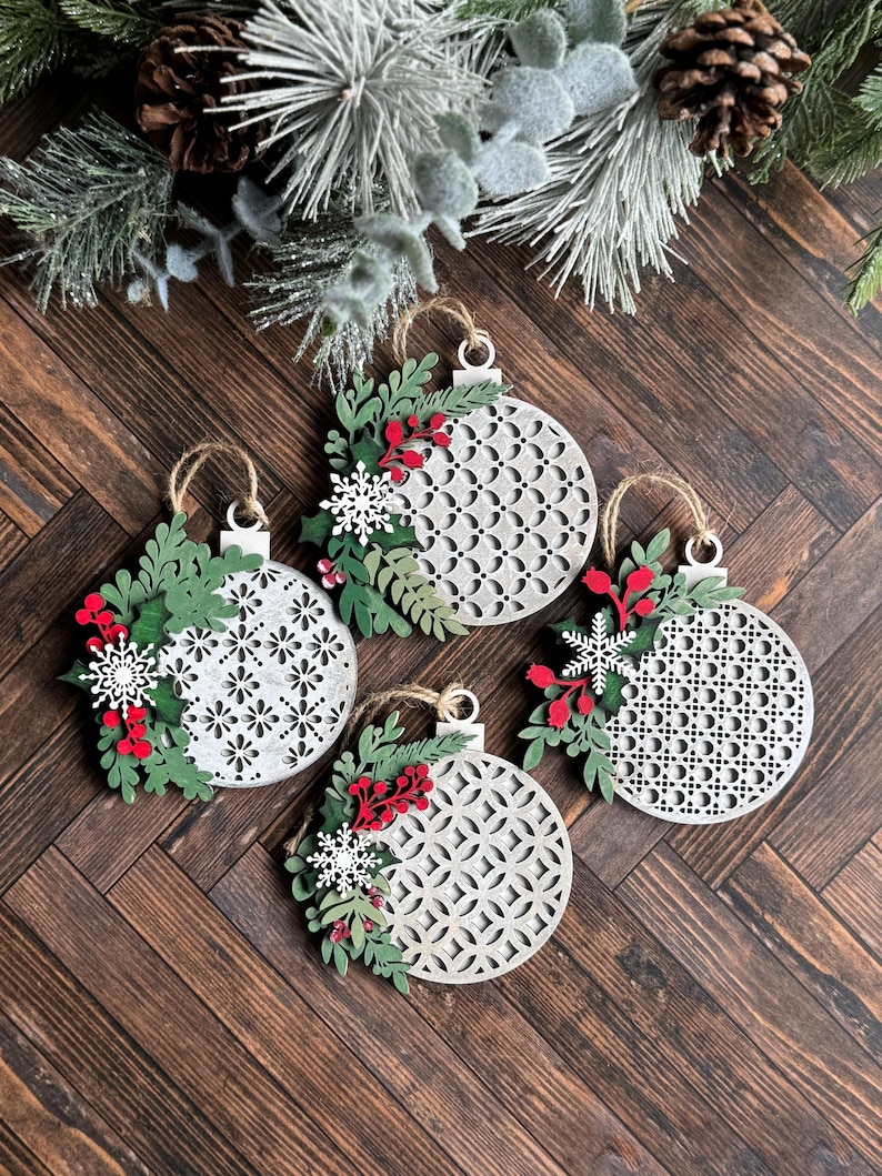May include: Four white wooden Christmas ornaments with a geometric pattern and red and green floral accents.