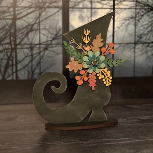 May include: A black wooden boot with a whimsical floral design. The boot is decorated with a variety of colorful flowers, leaves, and berries. The boot is a decorative piece for a home or office.