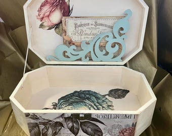 May include: A white wooden box with a hinged lid. The box is decorated with a floral design and a vintage label that reads "Fabrique de Serrurerie pour Batiments." The inside of the box is lined with a floral pattern.