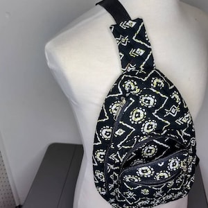 May include: A black and white patterned crossbody bag with a zippered pocket. The bag has a long adjustable strap.