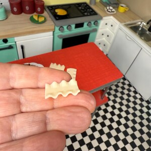 Puede incluir: Una sola pieza de pasta para lasa&ntilde;a, con bordes ondulados, se sostiene en una mano sobre un fondo de cuadros blancos y negros.