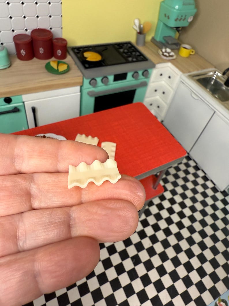 Puede incluir: Una sola pieza de pasta para lasa&ntilde;a, con bordes ondulados, se sostiene en una mano sobre un fondo de cuadros blancos y negros.