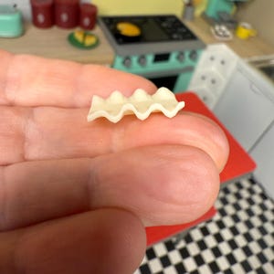 Puede incluir: Una sola pieza de pasta de lasa&ntilde;a sin cocinar, con un borde ondulado y acanalado, se sostiene en una mano.