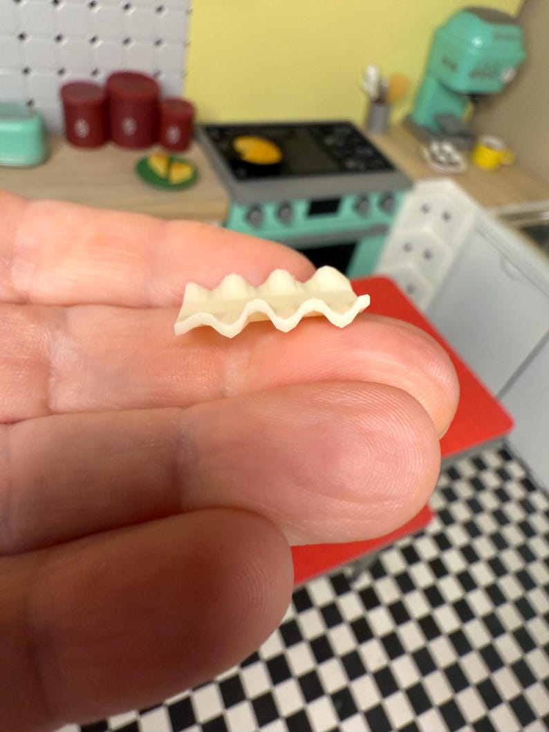 Puede incluir: Una sola pieza de pasta de lasa&ntilde;a sin cocinar, con un borde ondulado y acanalado, se sostiene en una mano.