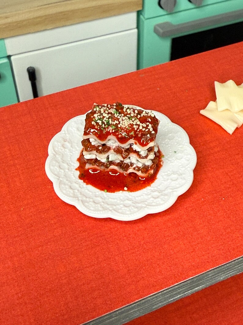 Puede incluir: Un peque&ntilde;o plato de lasa&ntilde;a cuadrado con tres capas de pasta, salsa de carne y queso. La lasa&ntilde;a est&aacute; cubierta con una pizca de hierbas verdes y una salsa roja.