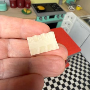 Puede incluir: Primer plano de una peque&ntilde;a hoja de papel rectangular, blanca y texturizada, con un patr&oacute;n de cuadr&iacute;cula.