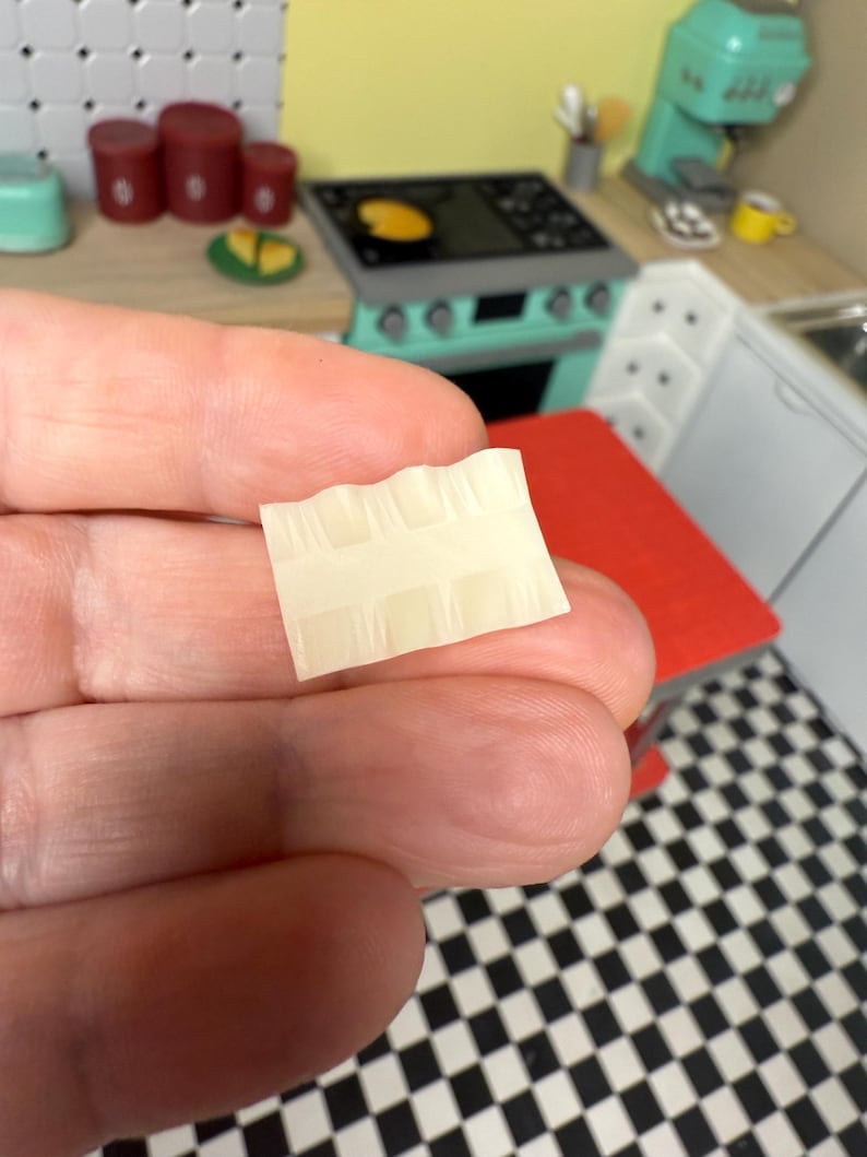 Puede incluir: Primer plano de una peque&ntilde;a hoja de papel rectangular, blanca y texturizada, con un patr&oacute;n de cuadr&iacute;cula.