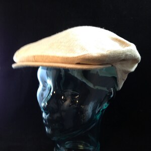 May include: A light beige cotton newsboy cap with a slightly curved brim.