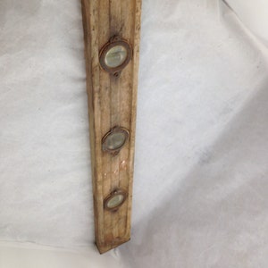 Puede incluir: Un nivel de madera vintage con tres niveles de burbuja de latón. El nivel es de madera y tiene un acabado desgastado. Los niveles de burbuja son de forma ovalada y tienen viales de vidrio.