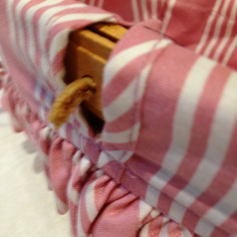 K&ouml;nnte beinhalten: Nahaufnahme eines rosa-wei&szlig; gestreiften Stoffes mit ger&uuml;schtem Rand. Der Stoff scheint ein Holzobjekt zu bedecken. Ein kleiner, hellbrauner Gegenstand ist sichtbar.