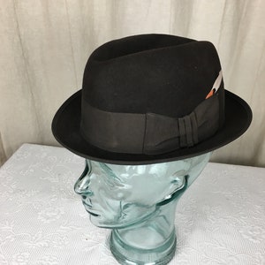 May include: A black fedora hat with a black ribbon and a small feather accent.