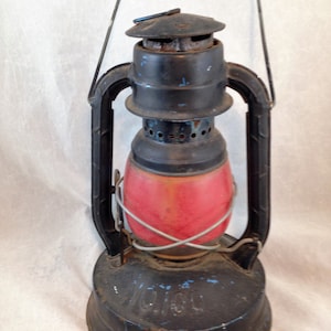 May include: A vintage black and red kerosene lantern with a metal handle and a glass globe. The lantern has a blue painted inscription that reads "VICTOR".