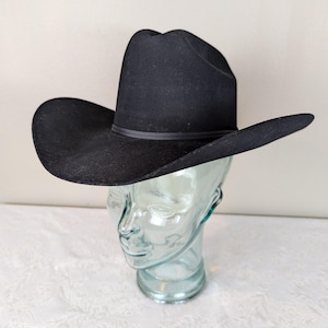Pode incluir: Um chapéu de cowboy de feltro preto com uma aba larga. O chapéu está em uma cabeça de manequim.